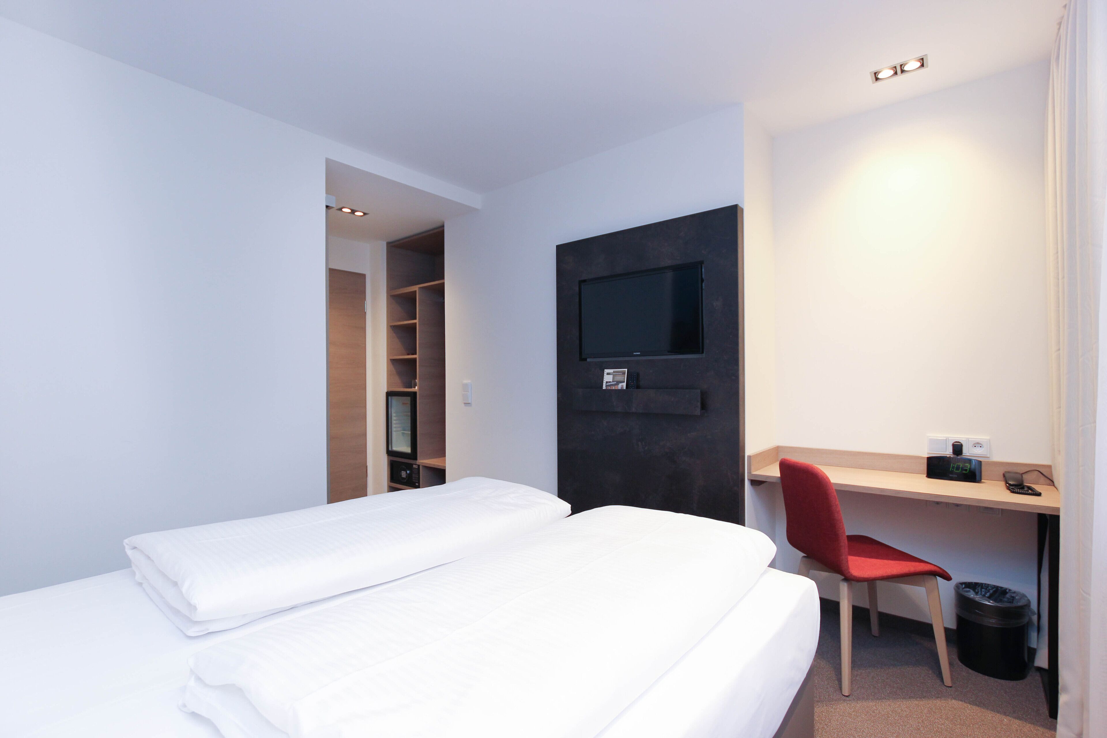 A hotel room with two beds, a desk with a chair, a TV, and a small trash bin.