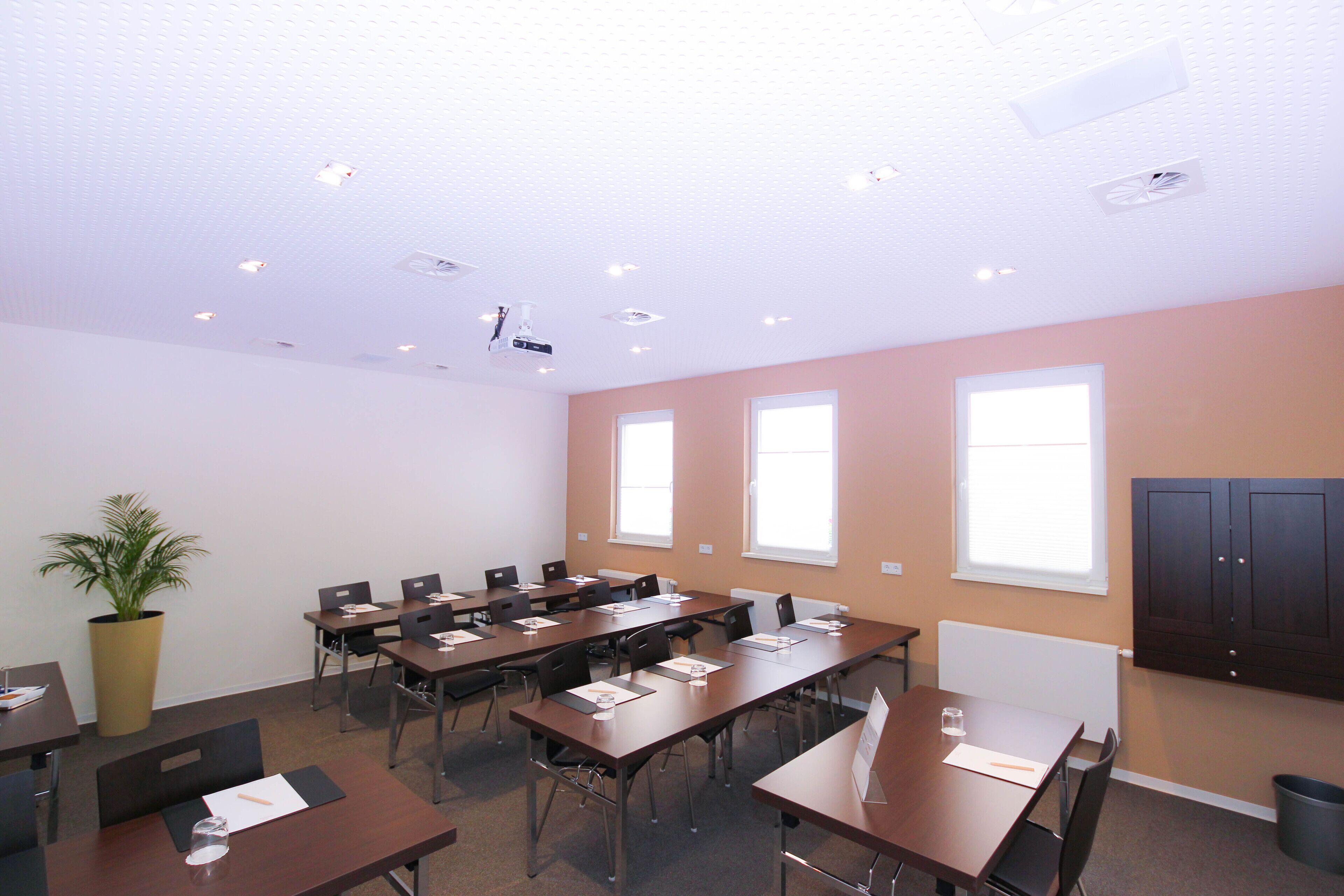 A conference room with multiple tables and chairs, a projector, and a potted plant.