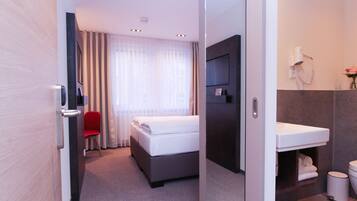 Habitación de hotel con cama, una silla roja, televisor, baño con lavamanos, inodoro y ducha.