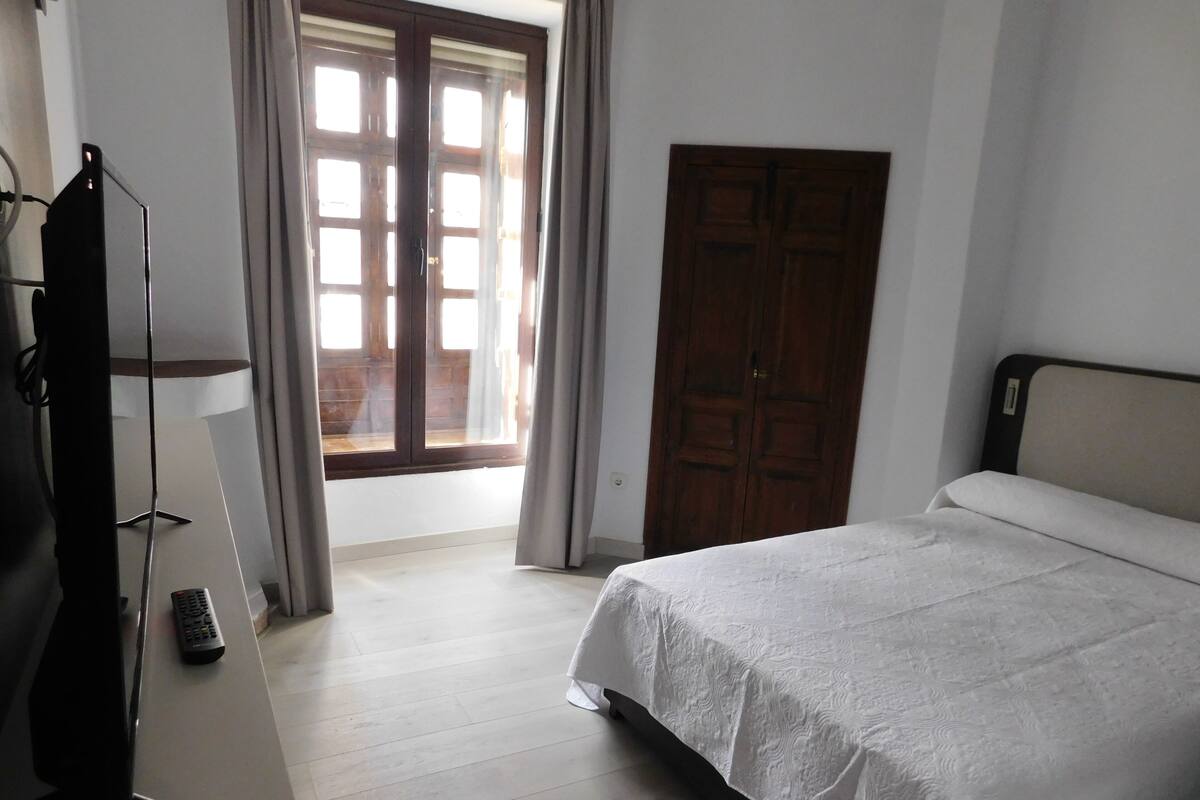 A bedroom with a bed, a wardrobe, a desk with a lamp, and a window with curtains.