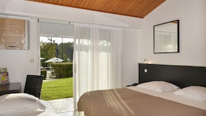 Un dormitorio con cama, escritorio y silla. Hay una puerta corrediza de vidrio que da a un balcón con vistas al exterior.