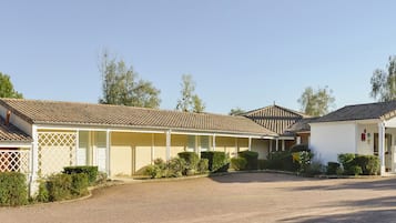 A row of two-story buildings with a tiled roof, a covered driveway, and a parking area with a scooter and a van.