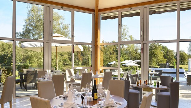 Un restaurante con ventanas amplias, mesas al aire libre y vistas a la vegetación.