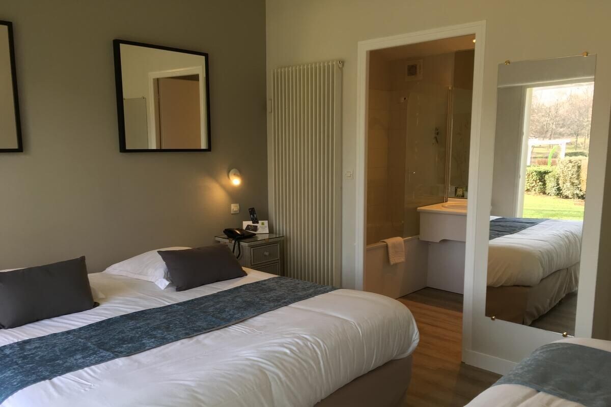 Habitación de hotel con dos camas, una mesita de noche, un espejo y vistas al jardín.
