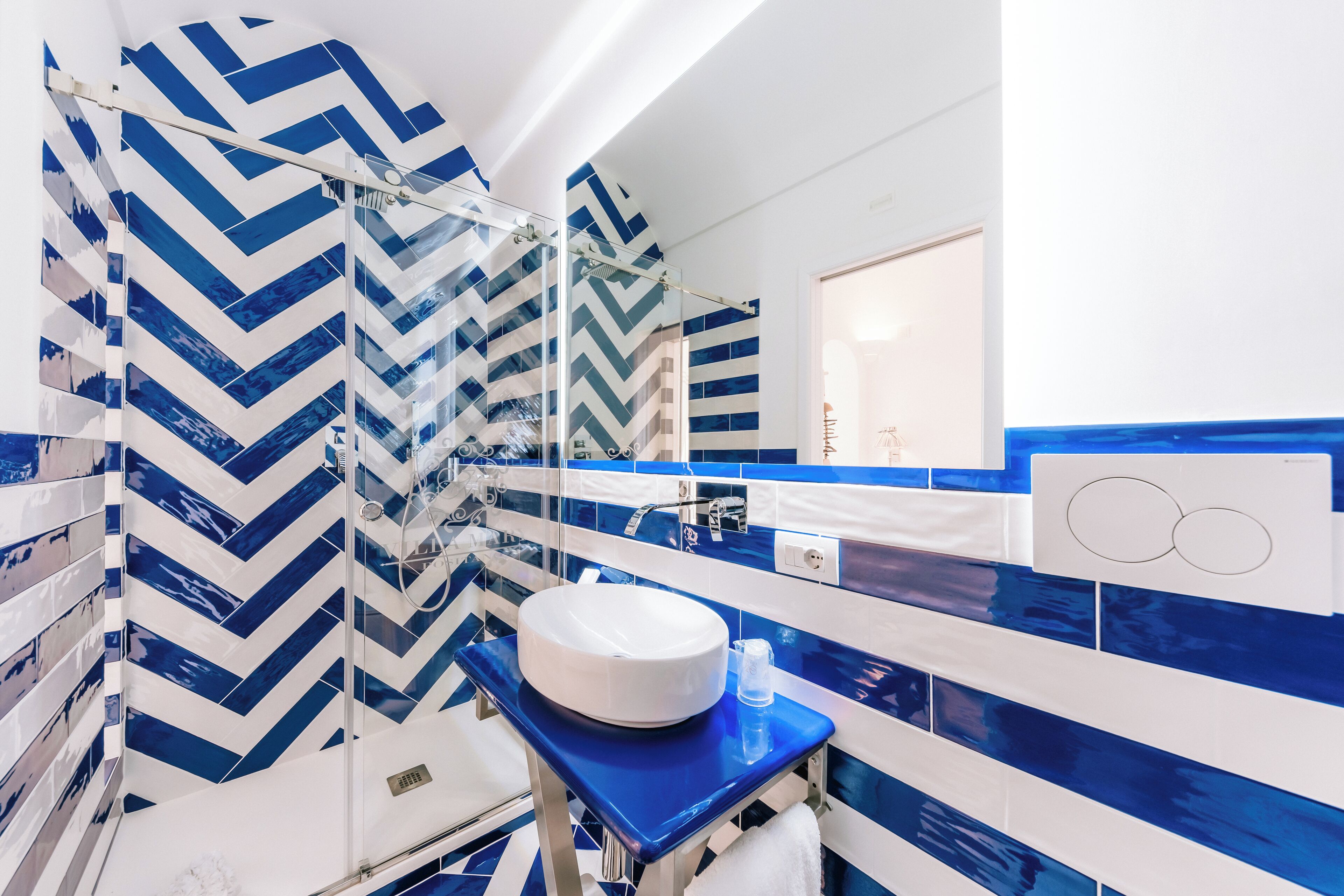 A modern bathroom with a large mirror, a round sink, and blue and white chevron-patterned tiles.