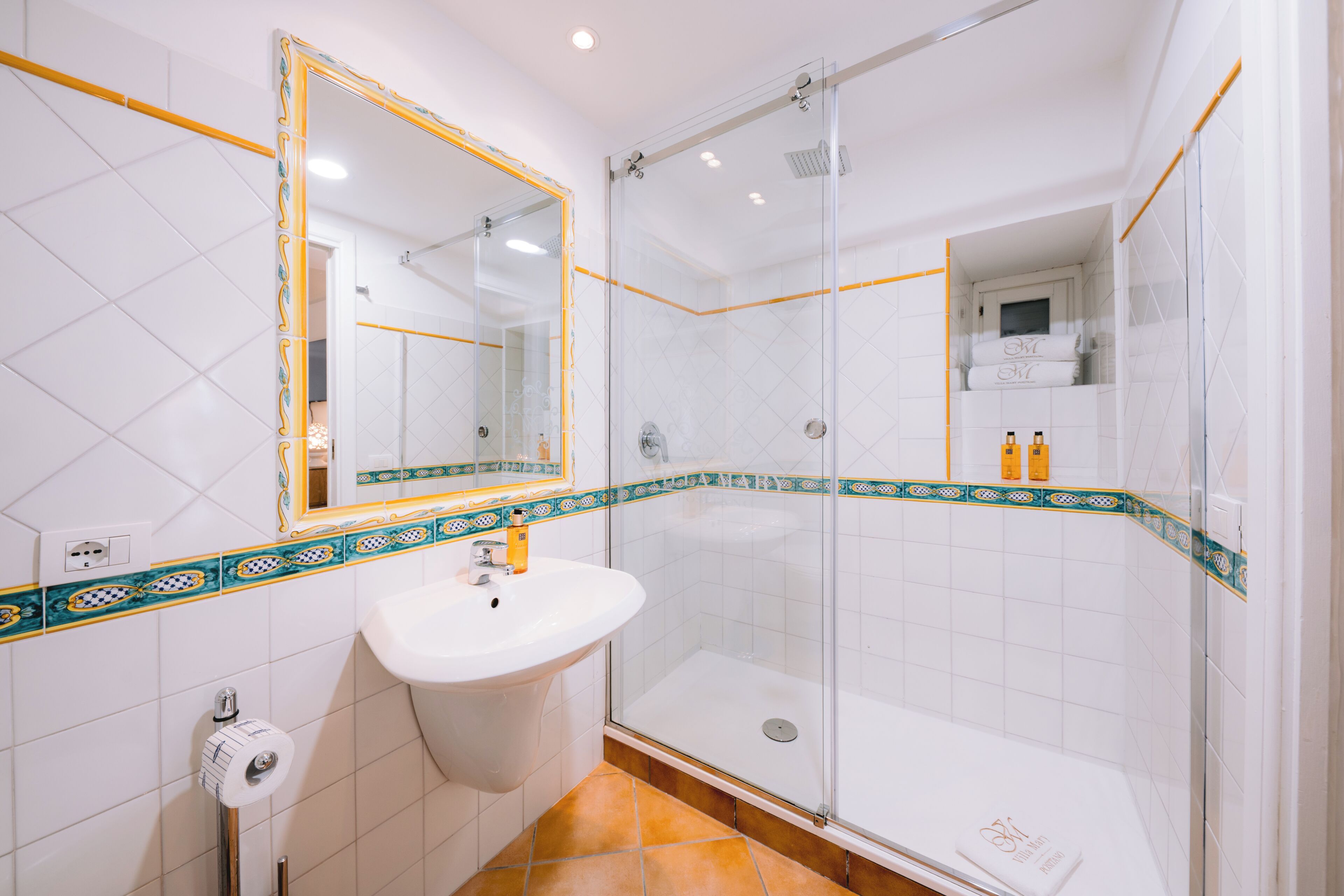 A bathroom with a glass-enclosed shower, a sink, and a mirror with a decorative frame.