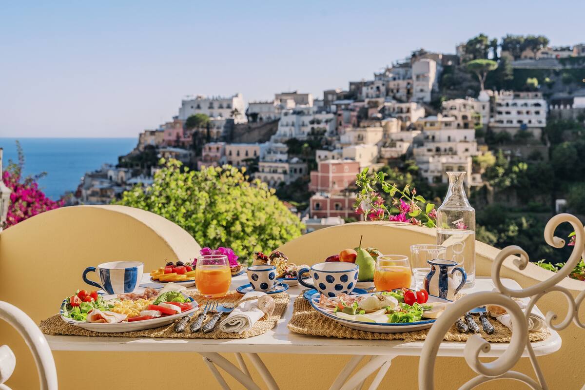 Una mesa preparada con alimentos para el desayuno y vista a un pueblo costero.