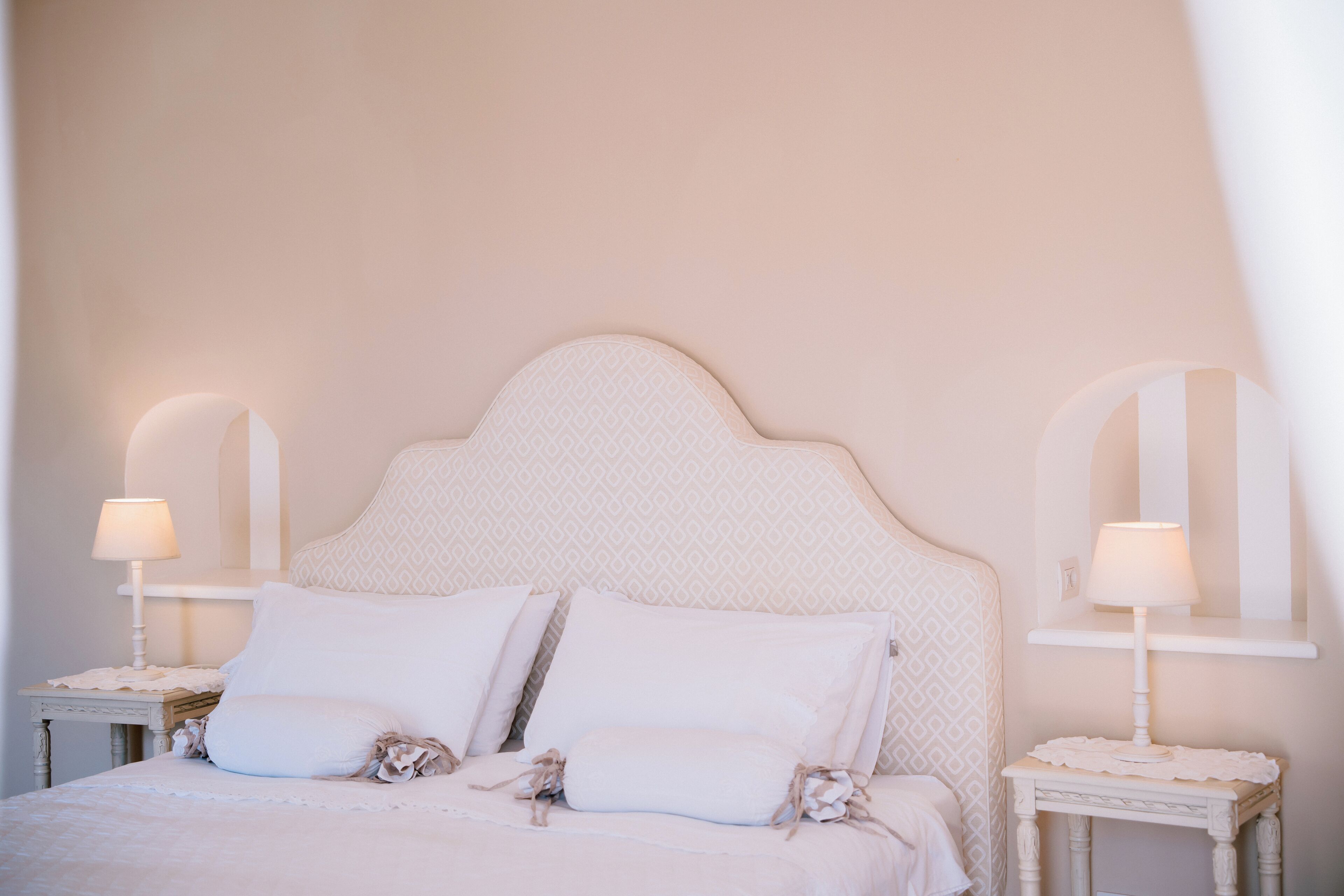 A neatly made bed with white linens and pillows, two bedside tables with lamps, and a patterned headboard.