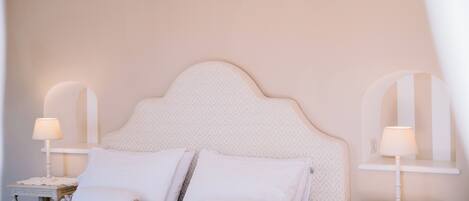 A neatly made bed with white linens and pillows, two bedside tables with lamps, and a patterned headboard.