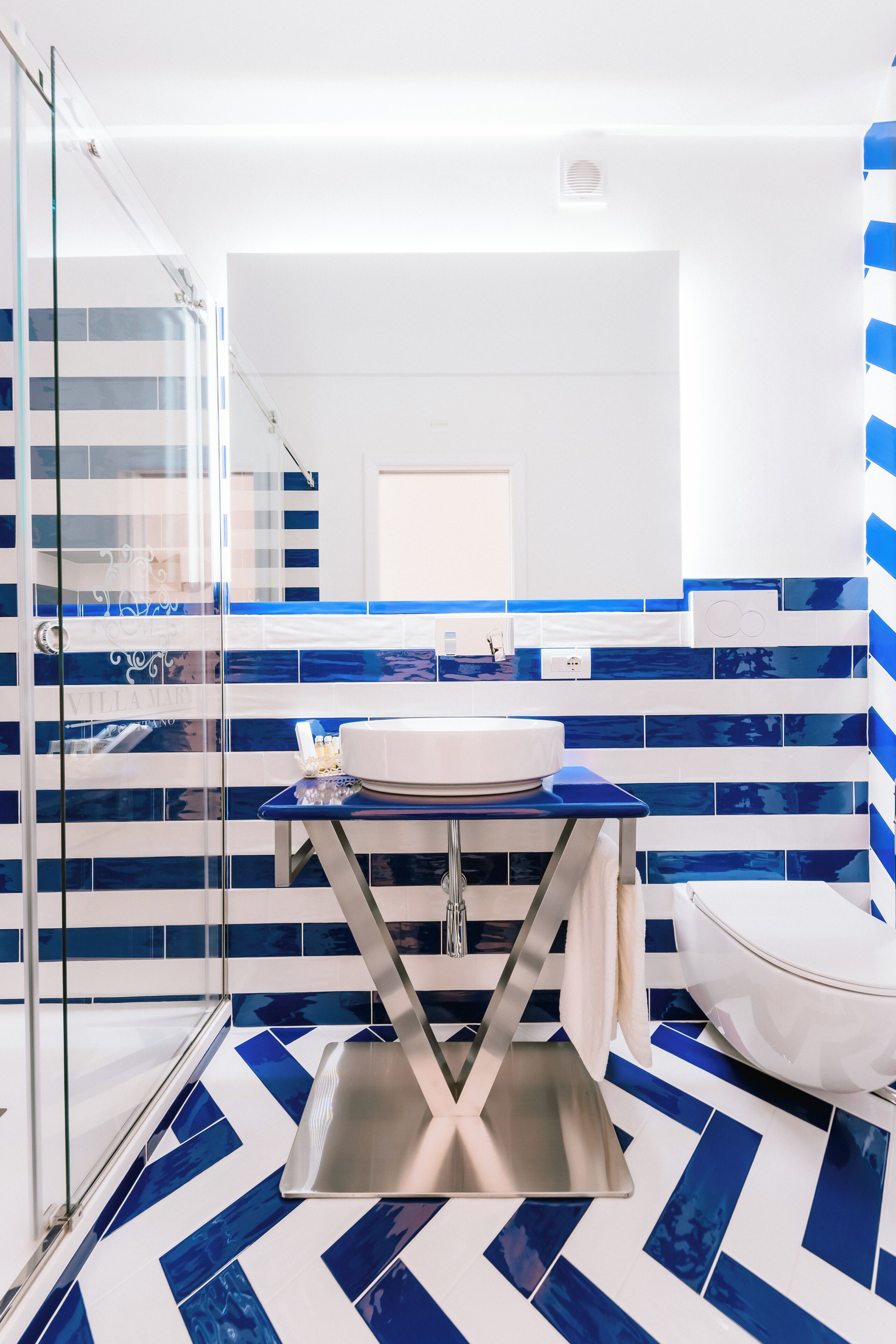 A modern bathroom with a glass shower enclosure, a white sink, and a blue and white tiled floor.