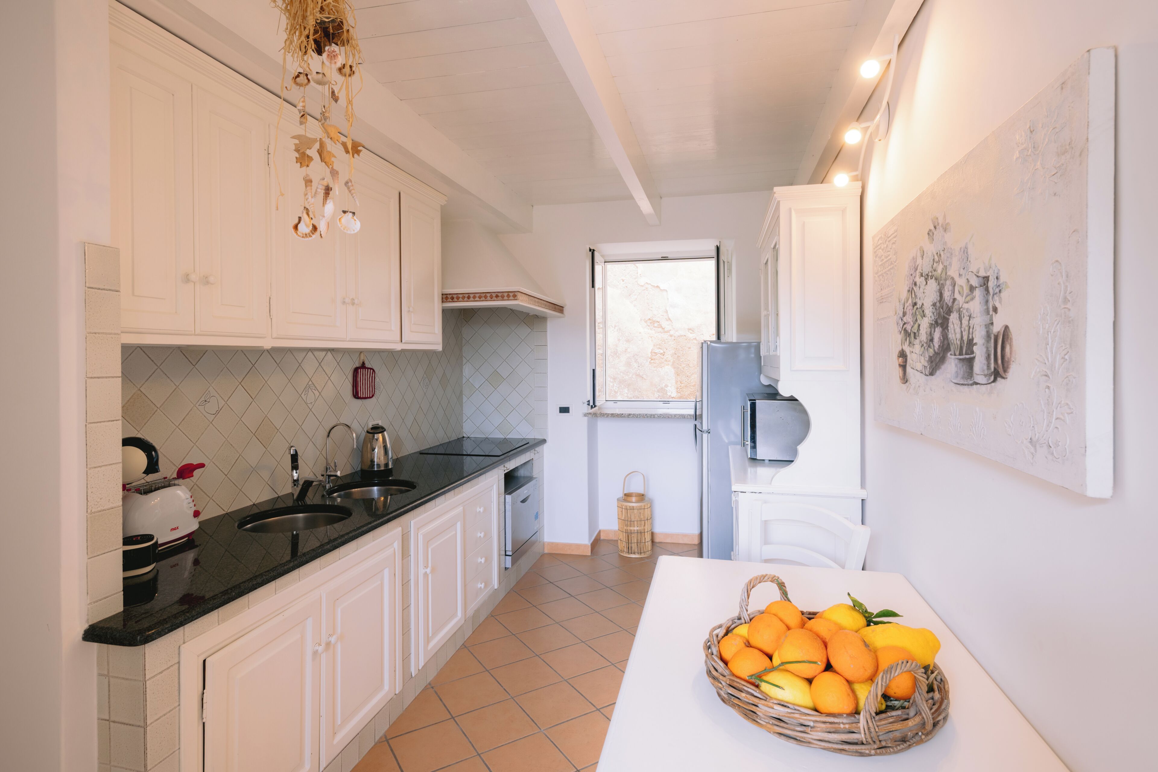 A kitchen with white cabinets, a black countertop, a sink, a microwave, and a window.