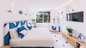 A modern bedroom with a large bed, a TV, and a window with a view of greenery. - Villa Mary Suites (Positano)