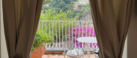 A balcony with a view of a hillside town, a white metal chair, and a potted plant.