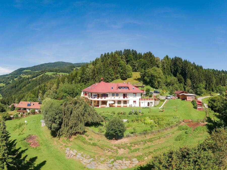 Ein großes Haus mit rotem Dach, umgeben von üppiger Vegetation und Hügeln.