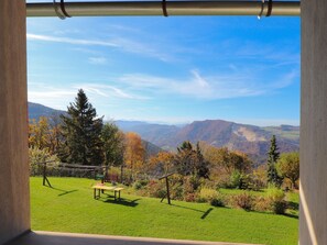 A view from a window overlooking a grassy area with a picnic table, trees, and mountains in the distance. - Biolandhaus Arche (Eberstein)