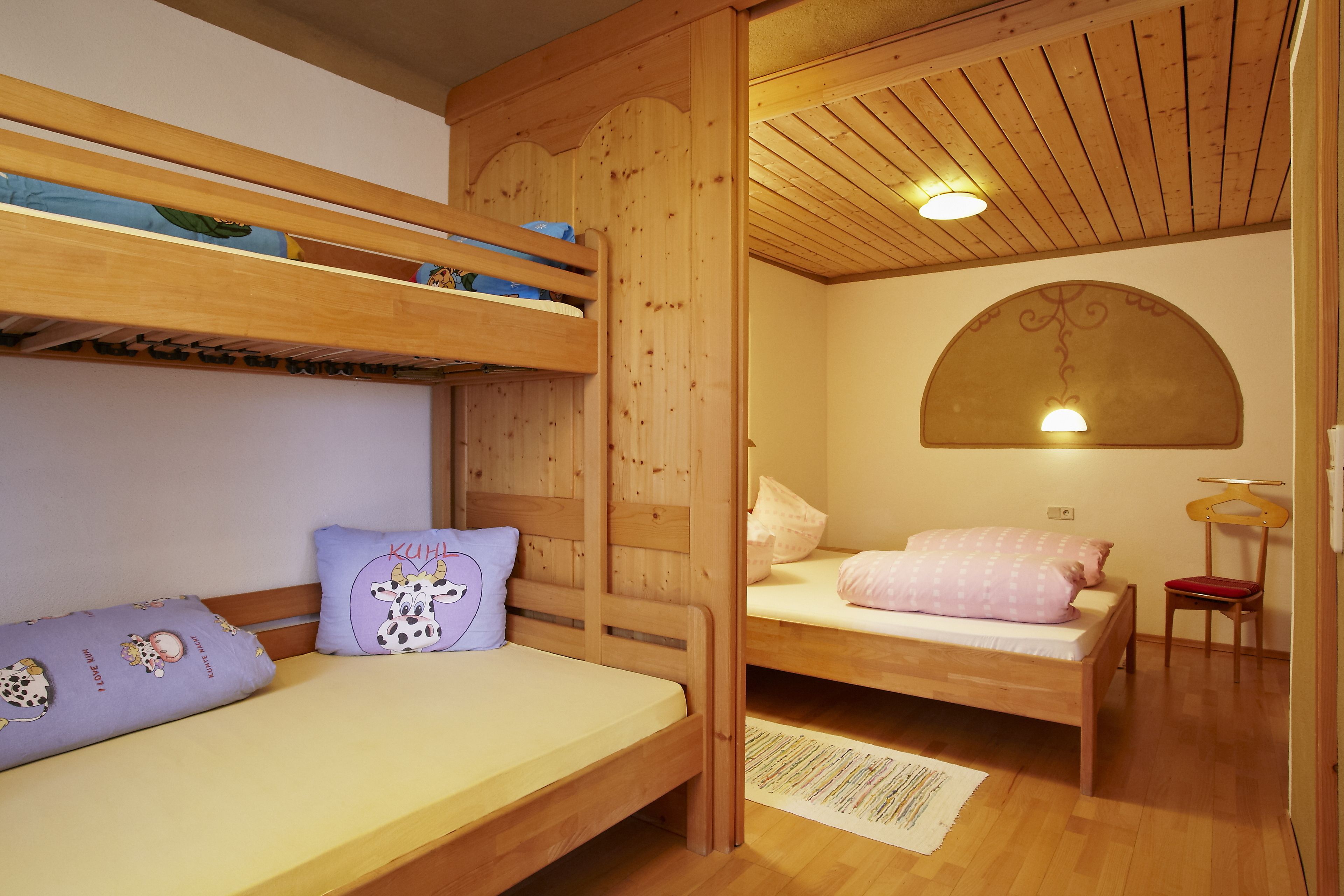 A room with two bunk beds, a single bed, wooden walls, a ceiling fan, and a hanging light fixture.
