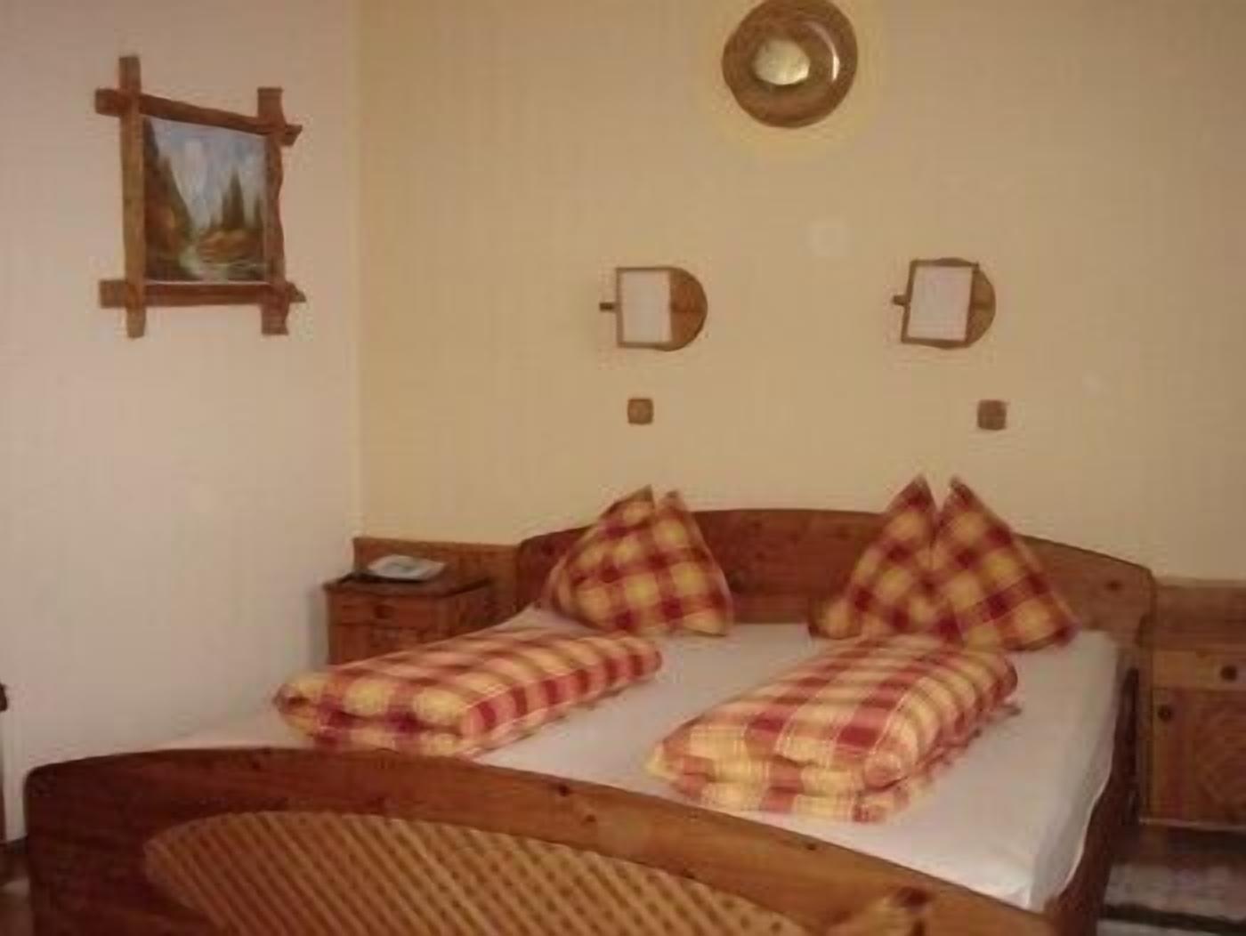 A room with a wooden bed, plaid bedding, a nightstand, and a wall-mounted picture.