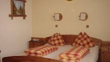 A room with a wooden bed, plaid bedding, a nightstand, and a wall-mounted picture.
