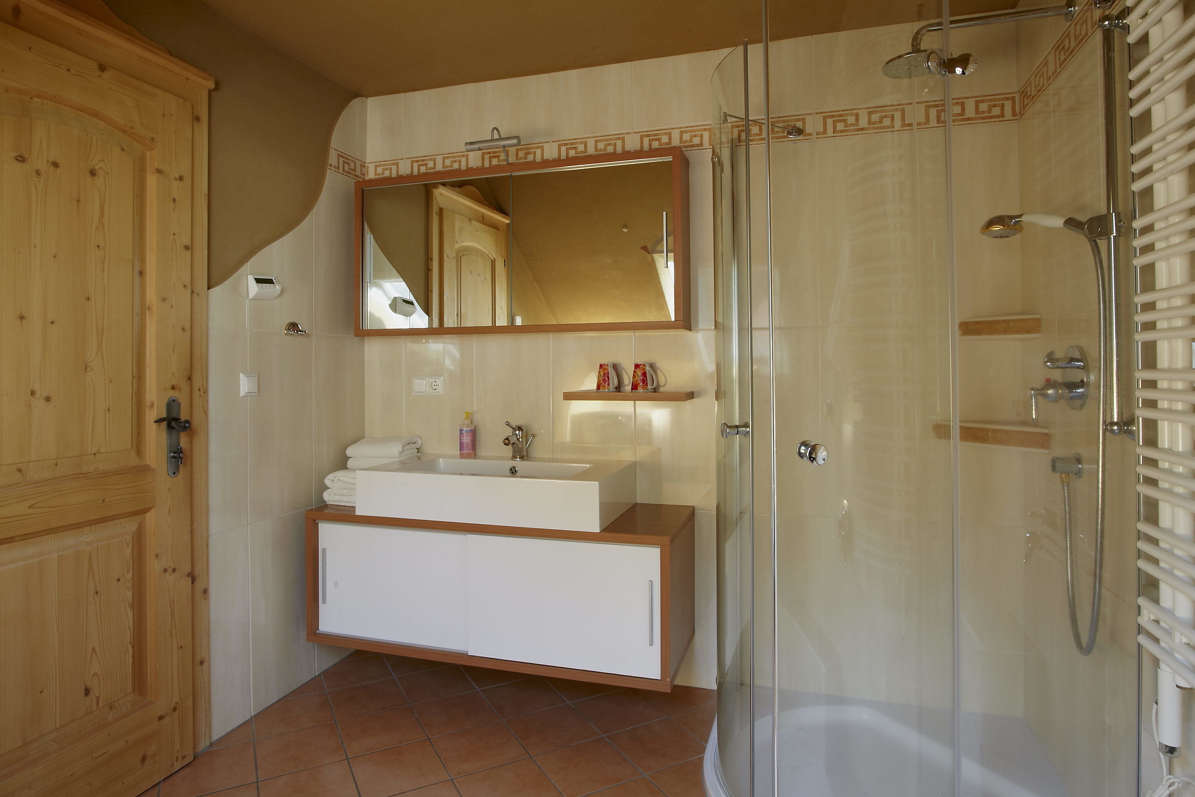 A bathroom with a wooden door, a white vanity with a mirror, a shower area, and a tiled floor.