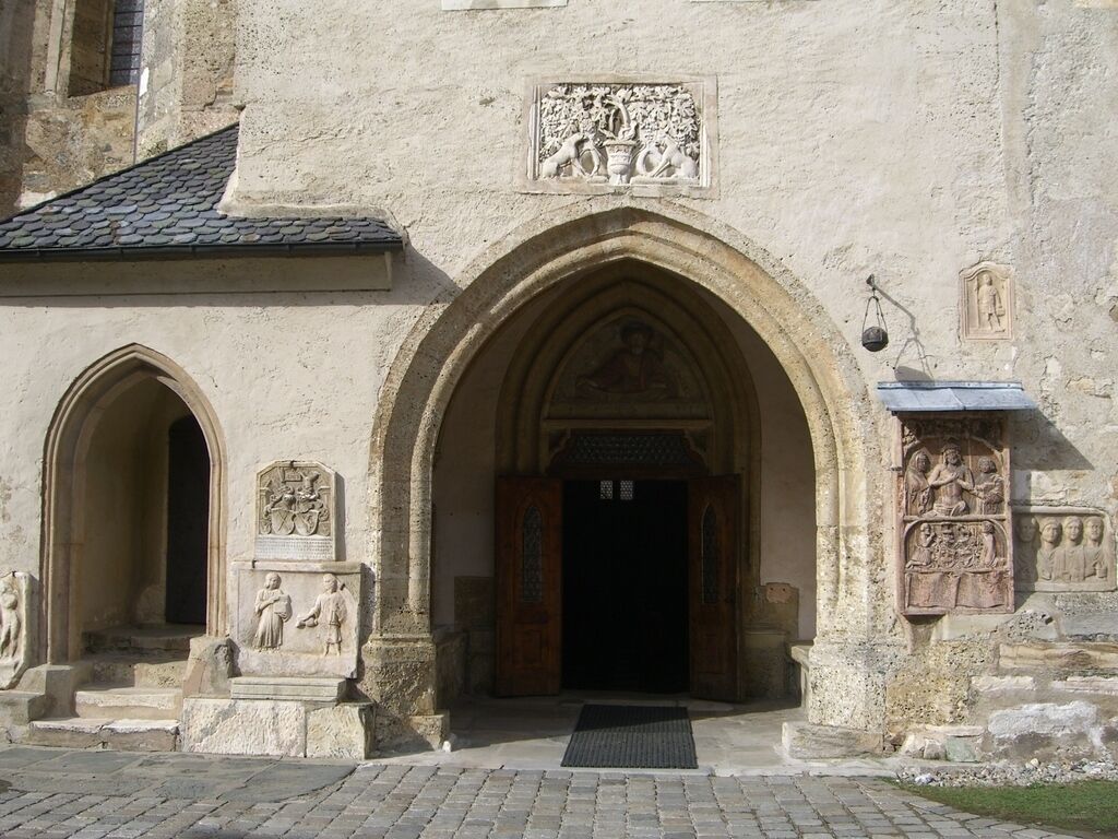 An entrance with a large arched doorway, stone carvings, and a small statue on the left.