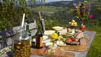 En picknickuppsättning med ett träbord, en burk med oliver, en flaska vin, en vas med blommor och diverse matvaror.