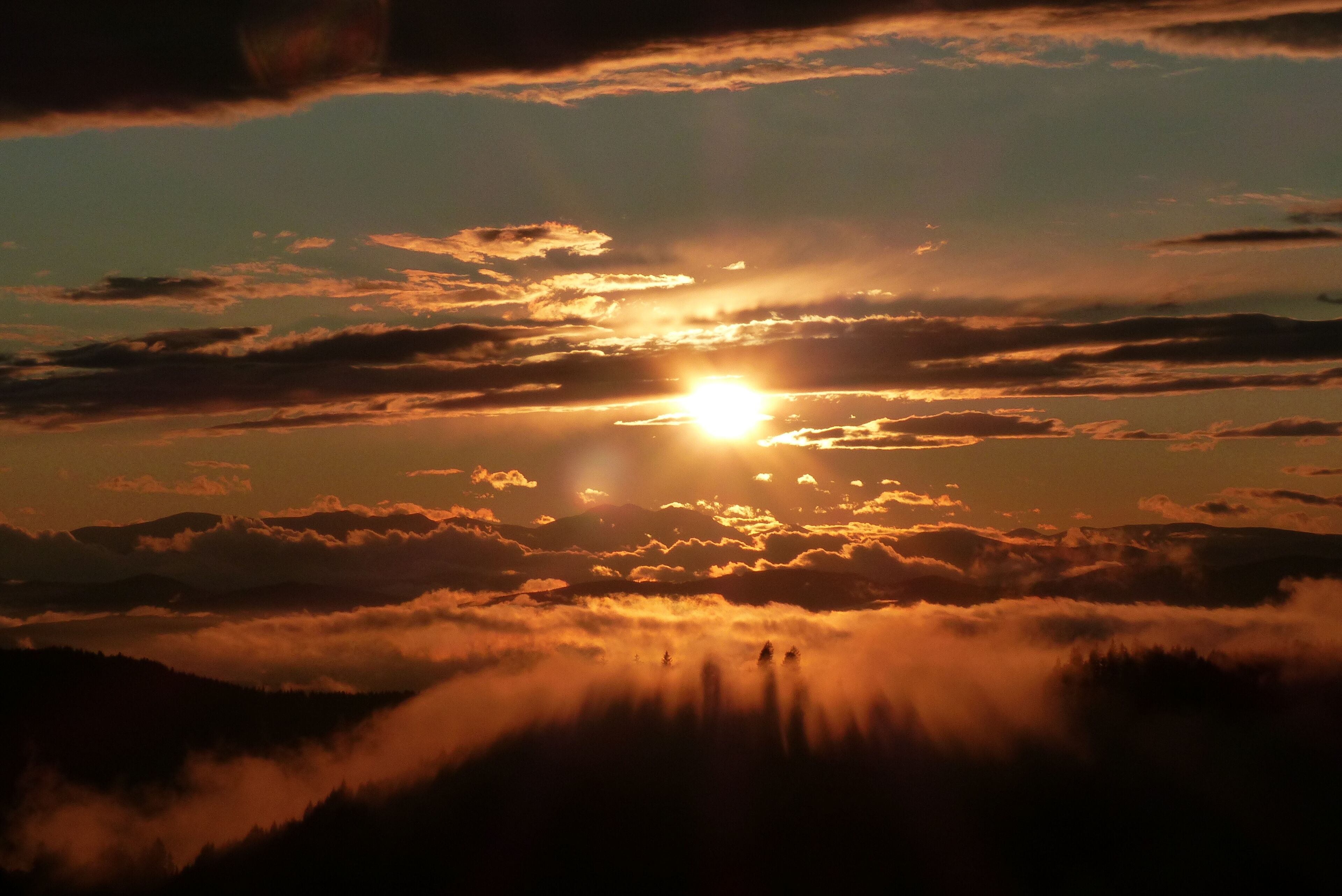 Een zonsondergang boven een bergachtig landschap met wolken.