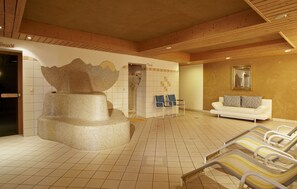 A spa area with a large decorative wall, a white sofa, and lounge chairs. - Biolandhaus Arche (Eberstein)