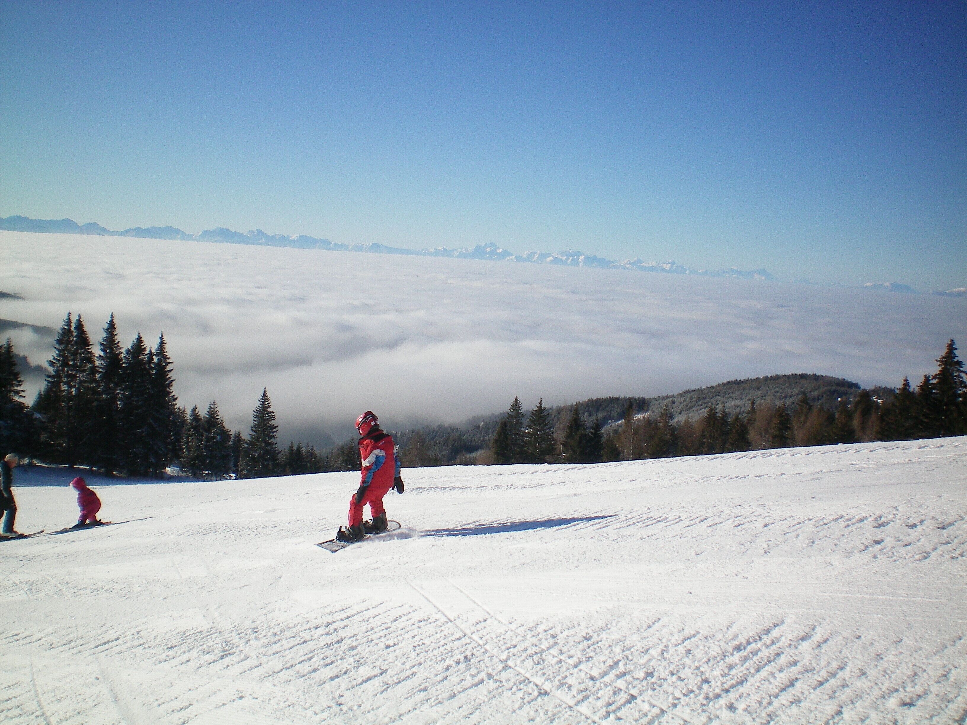 A snowy mountain landscape with a snowboarder in the foreground and a skier in the background.
