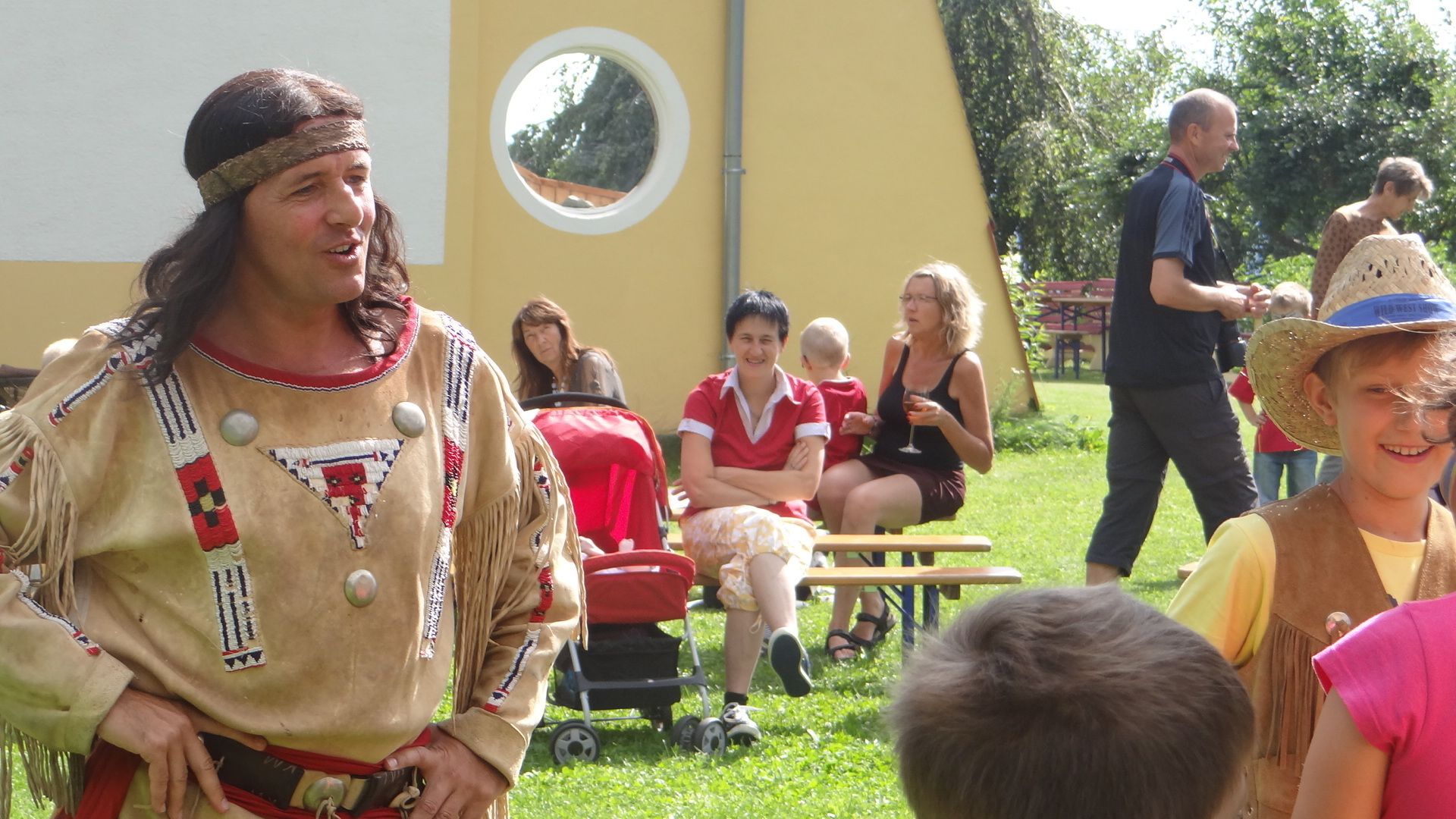 A group of people in an outdoor setting with a yellow building and a circular window.