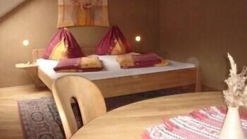 A cozy room with a bed, a table, and a chair. There is a painting on the wall and a vase on the table.