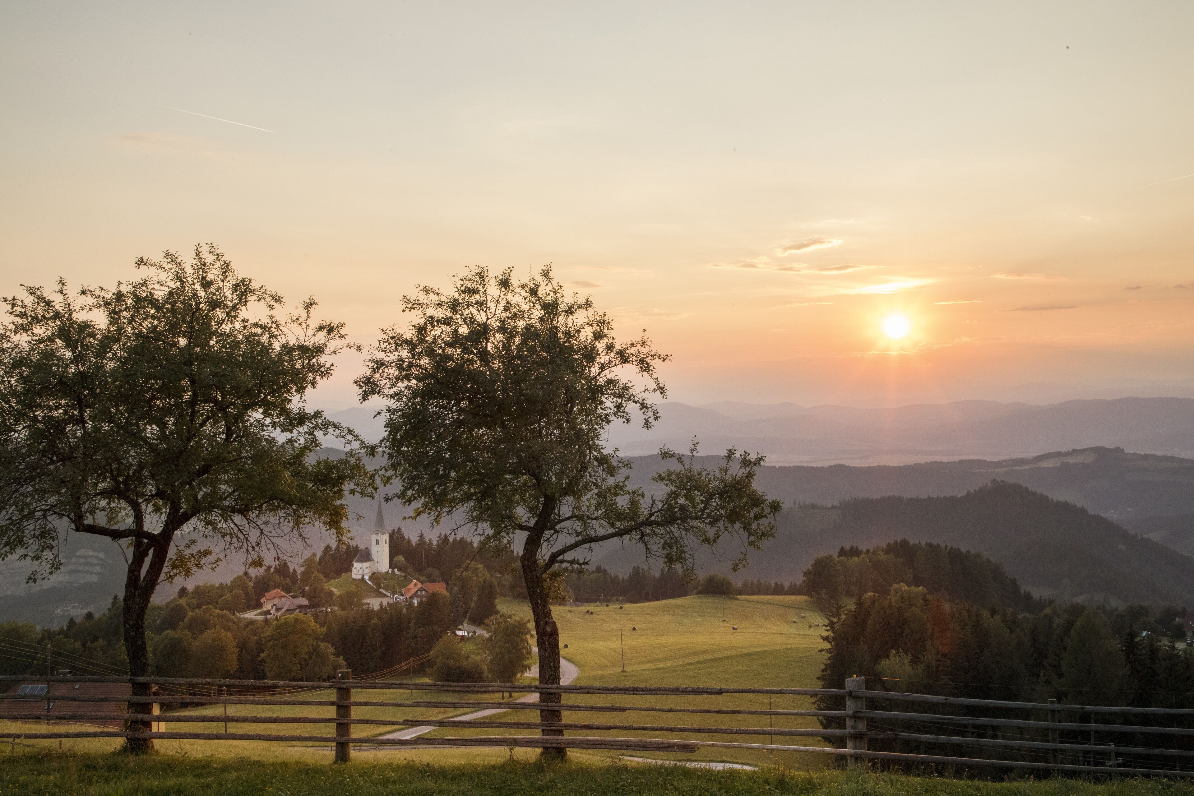 A rural landscape with a church, trees, and a fence.