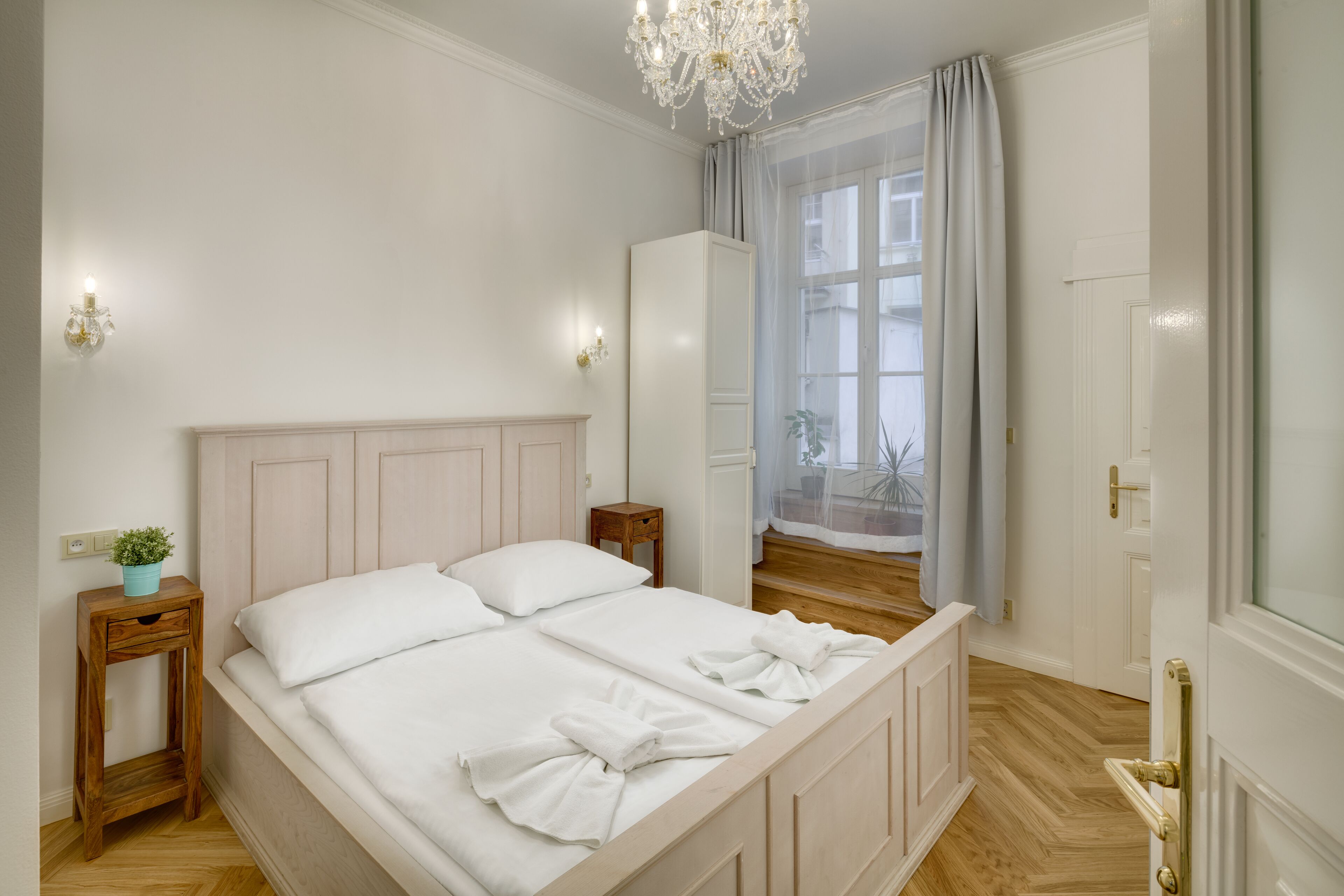 Quarto com uma cama grande, uma mesa de cabeceira com uma planta, um guarda-roupa e uma janela com cortinas.