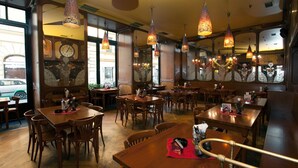 Interior de un restaurante con mesas y sillas de madera, lámparas colgantes y un ventanal con vistas a la calle.