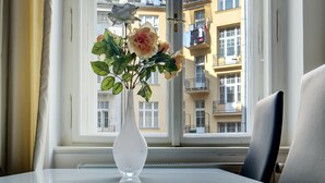 Una habitación con una mesa, un florero con flores y vistas a edificios a través de una ventana.