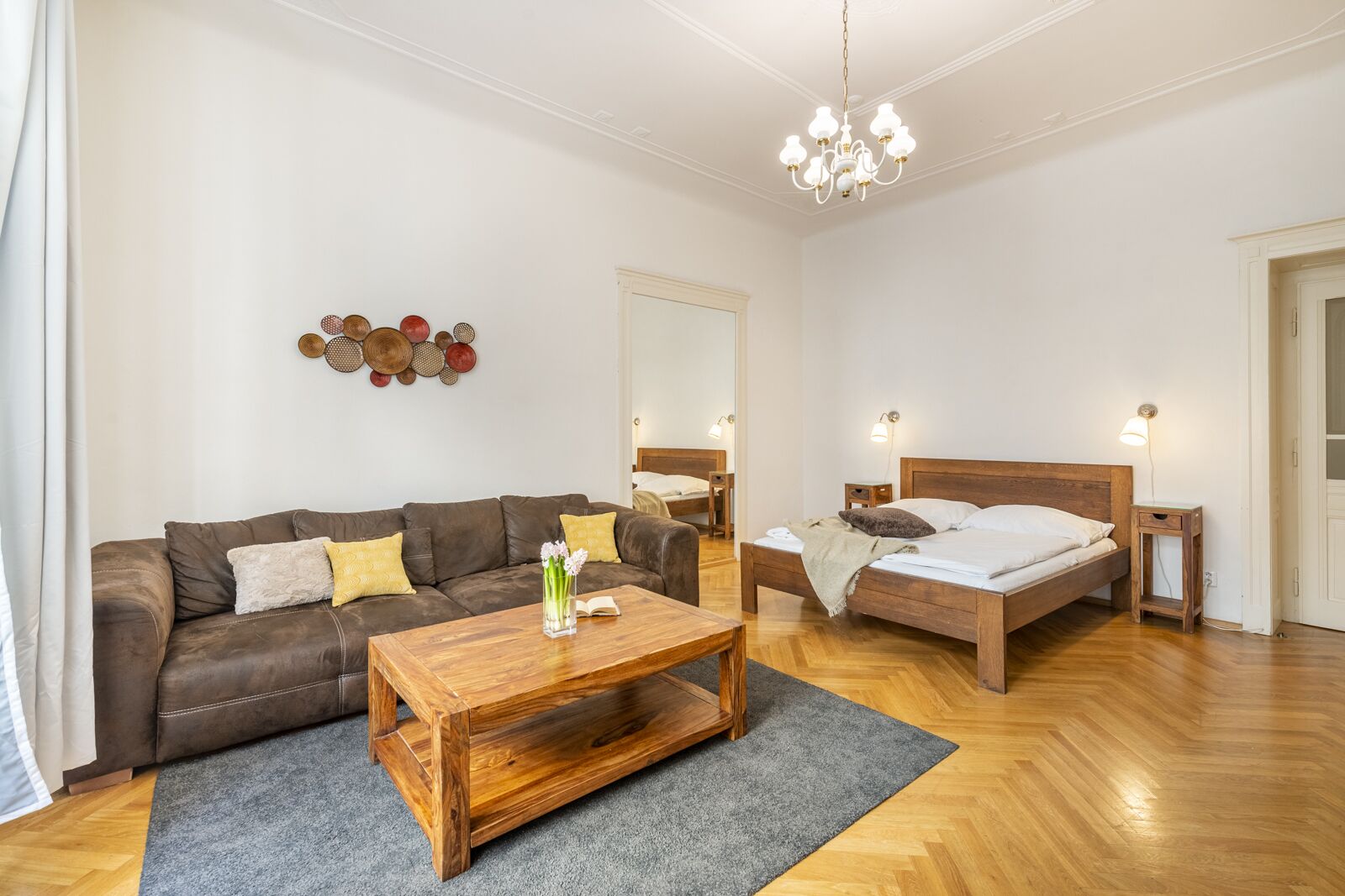 A modern bedroom with a wooden bed, a brown leather sofa, a wooden coffee table, and a chandelier.