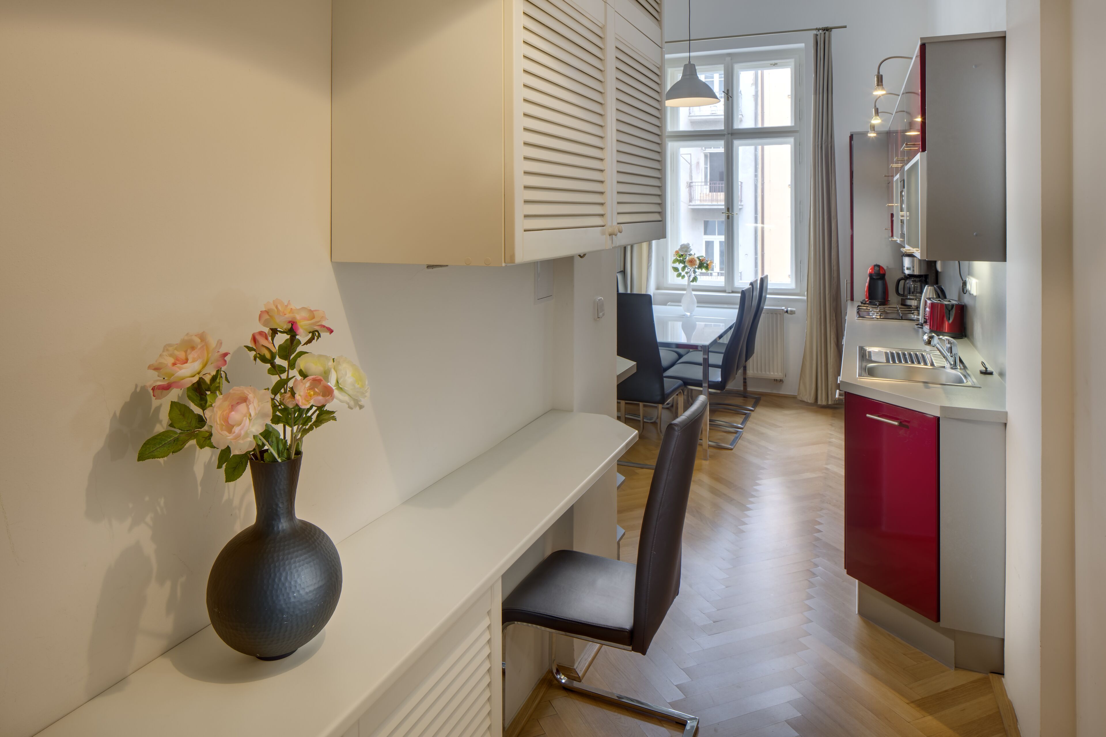 A modern kitchen with a red cabinet, a white countertop, and a vase of flowers on a shelf.