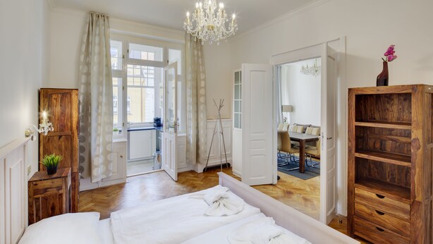 Un dormitorio con una cama grande, un armario de madera y vista al área de estar por una puerta abierta.