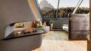 Una sala moderna con un sofá curvo, una mesita y vistas a un paisaje montañoso a través de amplios ventanales.
