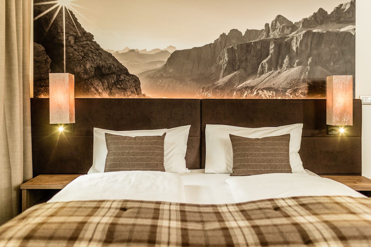 Une chambre d’hôtel avec un grand lit, deux lampes de chevet et une fresque murale représentant un paysage de montagne.