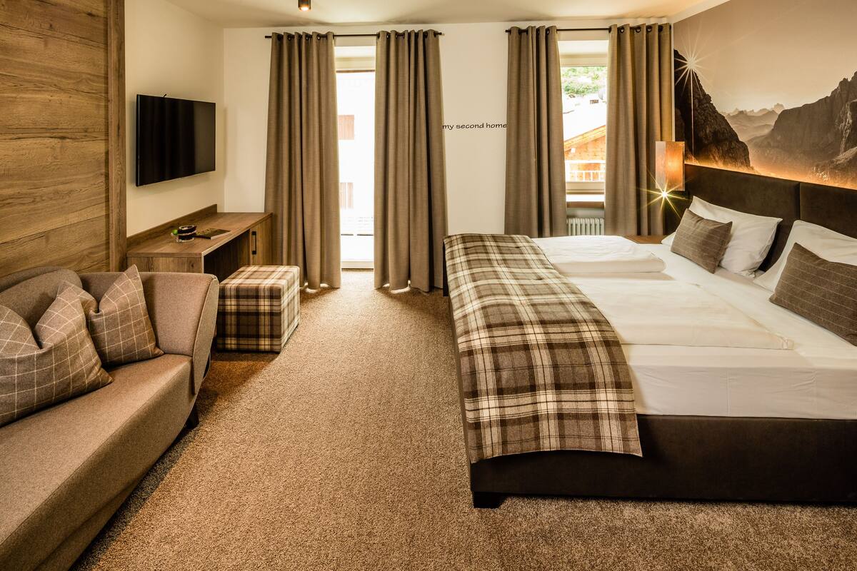 Une chambre à coucher avec un grand lit, un canapé, une télévision et une fenêtre avec des rideaux.