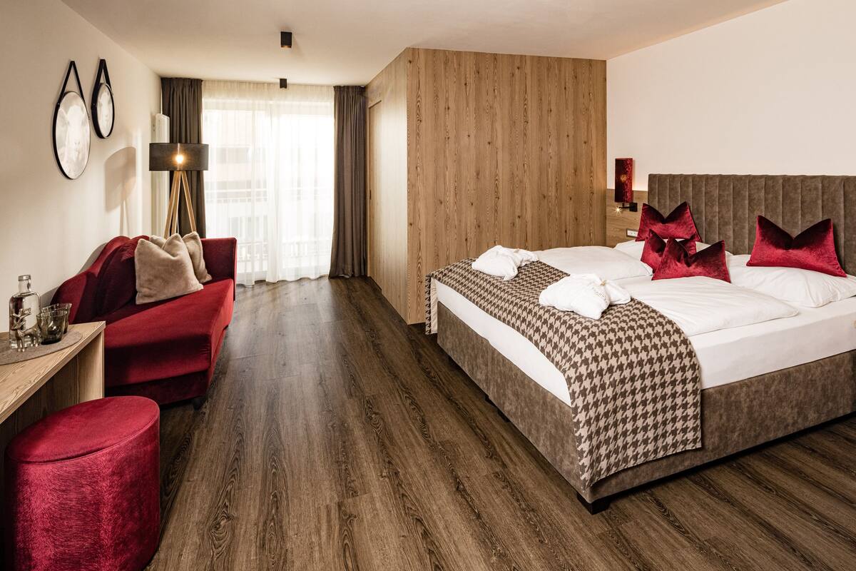 Une chambre d’hôtel avec un grand lit, un canapé rouge, un plancher en bois et un bureau avec une lampe.