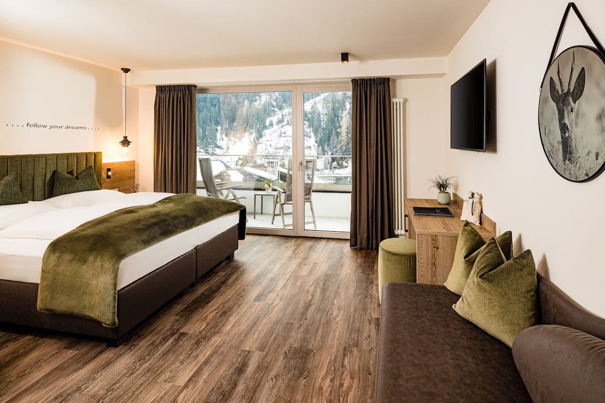 Une chambre d’hôtel avec un lit, un canapé, un bureau et une vue sur un paysage enneigé, visible à travers la porte vitrée.