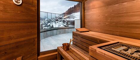 A wooden sauna with a large window offering a view of a snowy village.