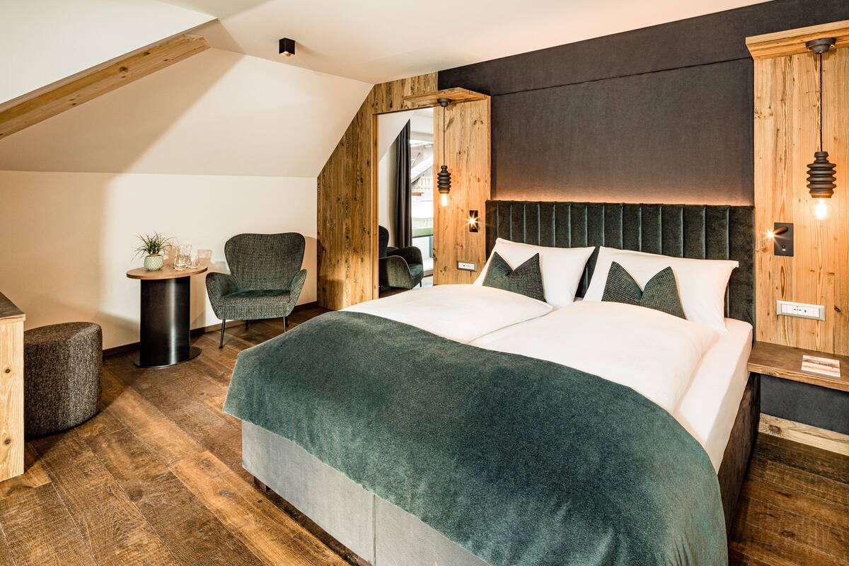 Une chambre à coucher avec un grand lit, une tête de lit en bois et une petite table sur laquelle est posée une plante.