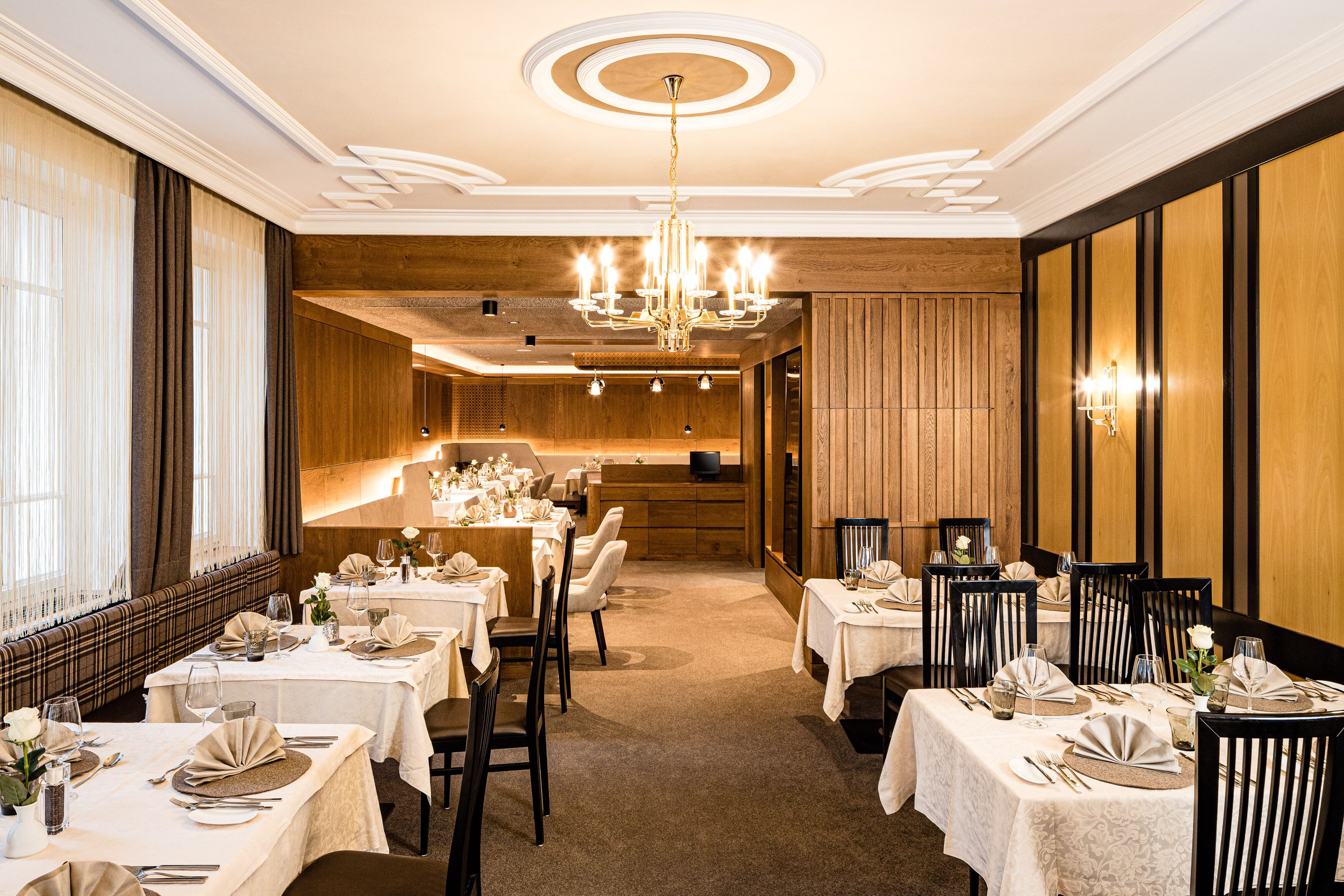 A formal dining room with multiple tables set for service, a chandelier, and wooden paneling on the walls.