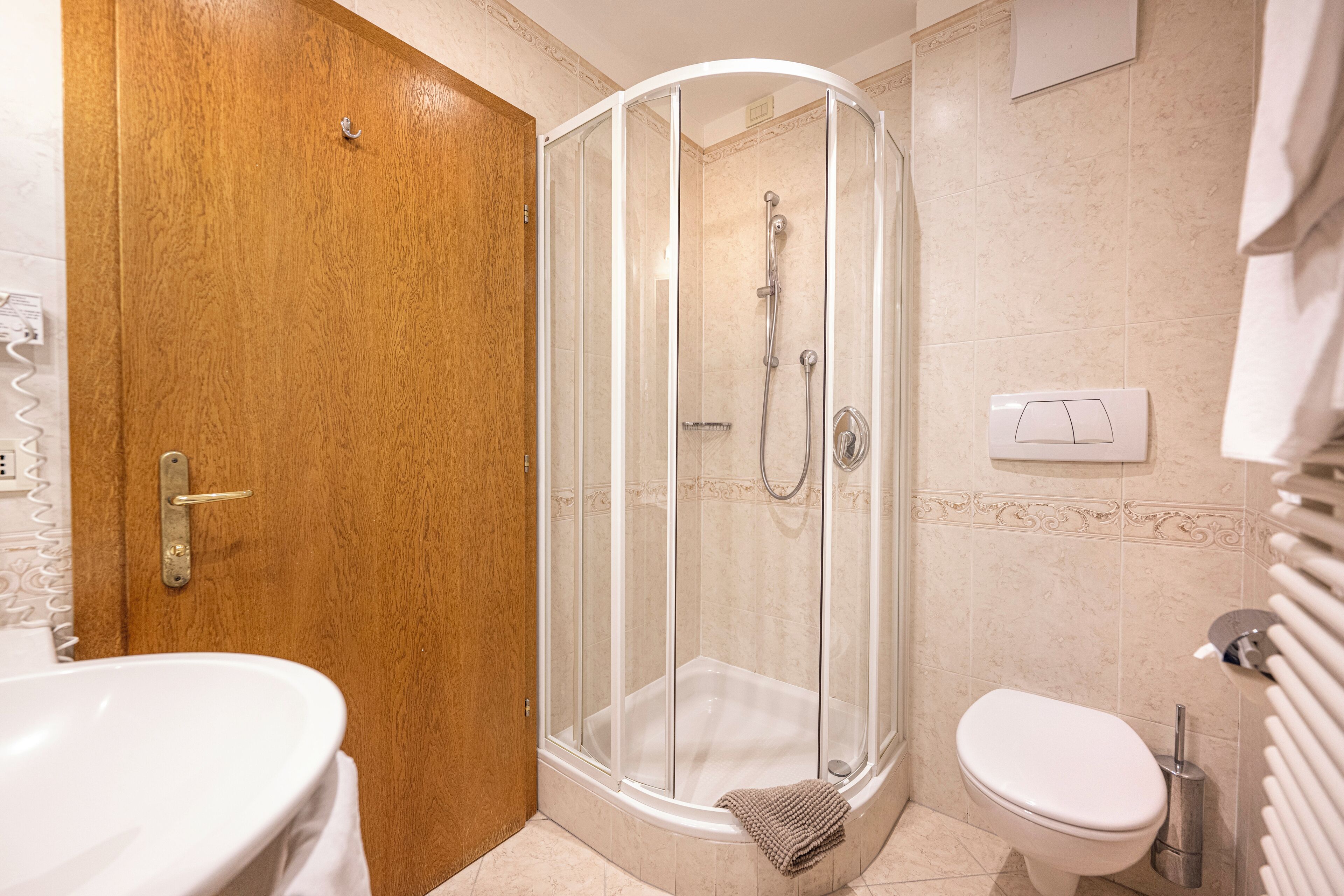 A bathroom with a wooden door, a glass shower enclosure, a white sink, and a toilet.