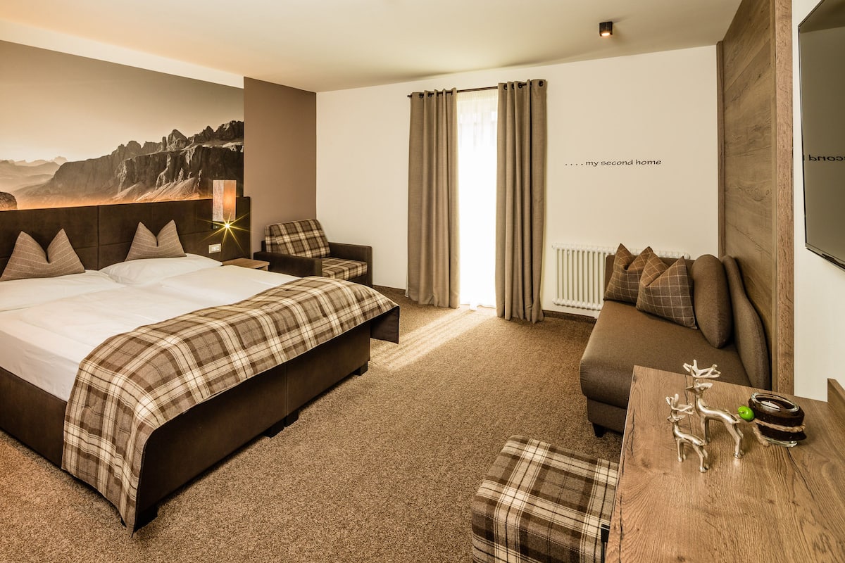 Une chambre d’hôtel avec un grand lit, un canapé, une petite table et un téléviseur fixé au mur.