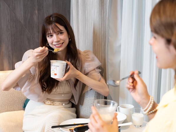 A person sitting at a table with a bowl, spoon, and a cup, with a window and curtains in the background. - Tokyu Stay Yotsuya Shinjuku Area (Tokyo)