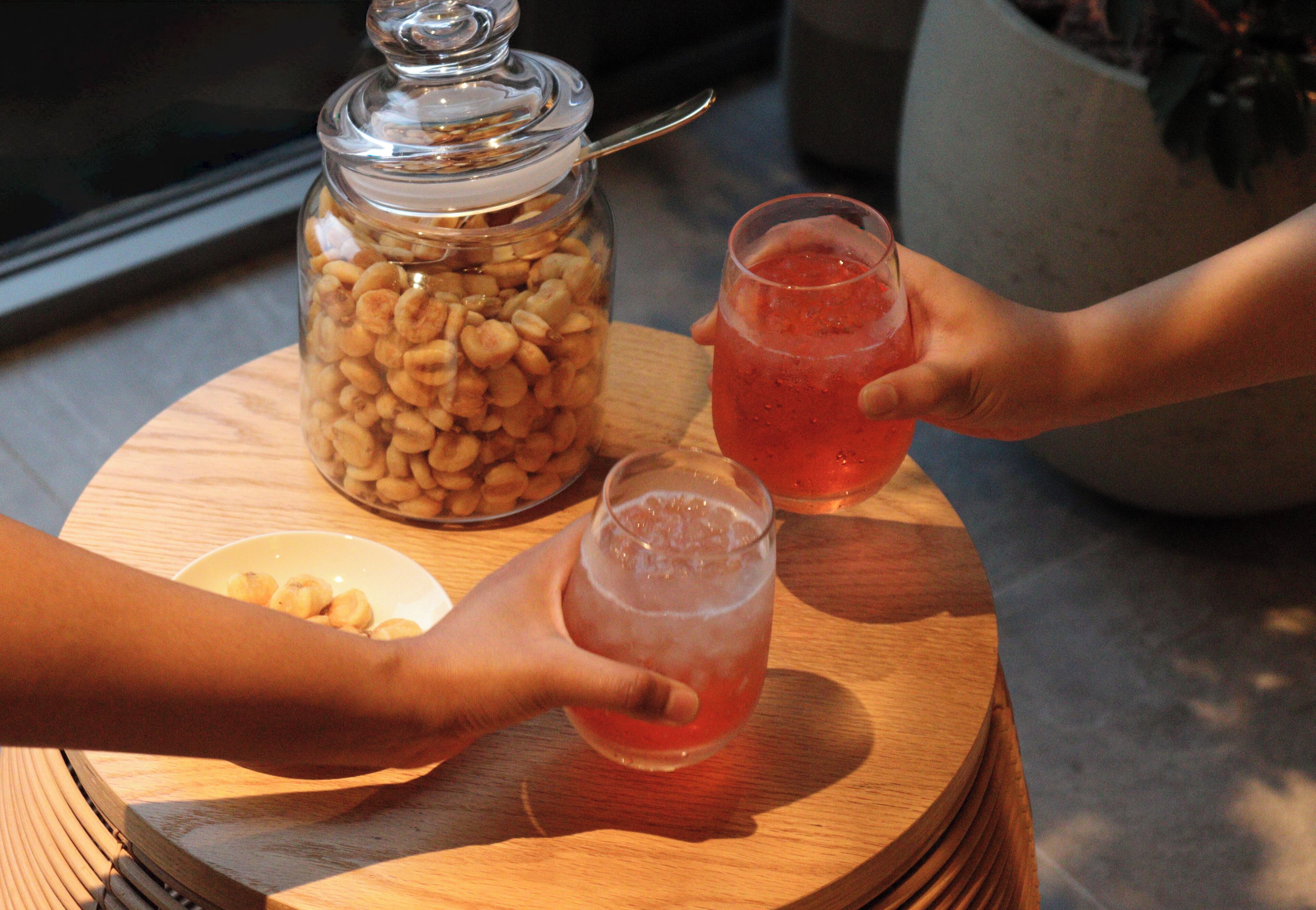 Una mesa de madera con un tarro de vidrio lleno de nueces, dos vasos de una bebida rosada y un tazón de nueces.