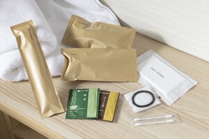 A wooden surface with various toiletries including a toothbrush, a hair brush, a tea bag, a body sponge, and cotton swabs.